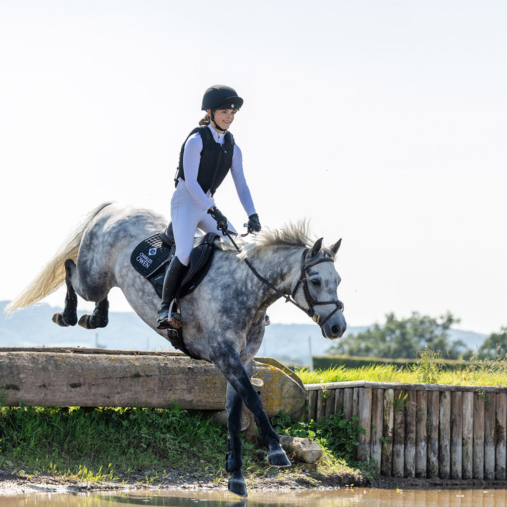 Person riding a horse over a water jump in an outdoor setting